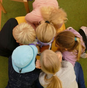 Fünf Schülerinnen und Schüler sitzen dicht beieinander und schauen gemeinsam auf ein Tablet.